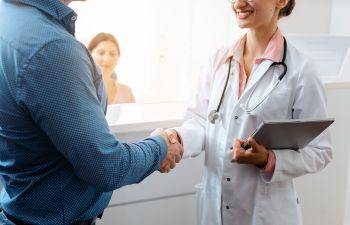 A doctor shaking hands while greeting a patient at a reception desk.